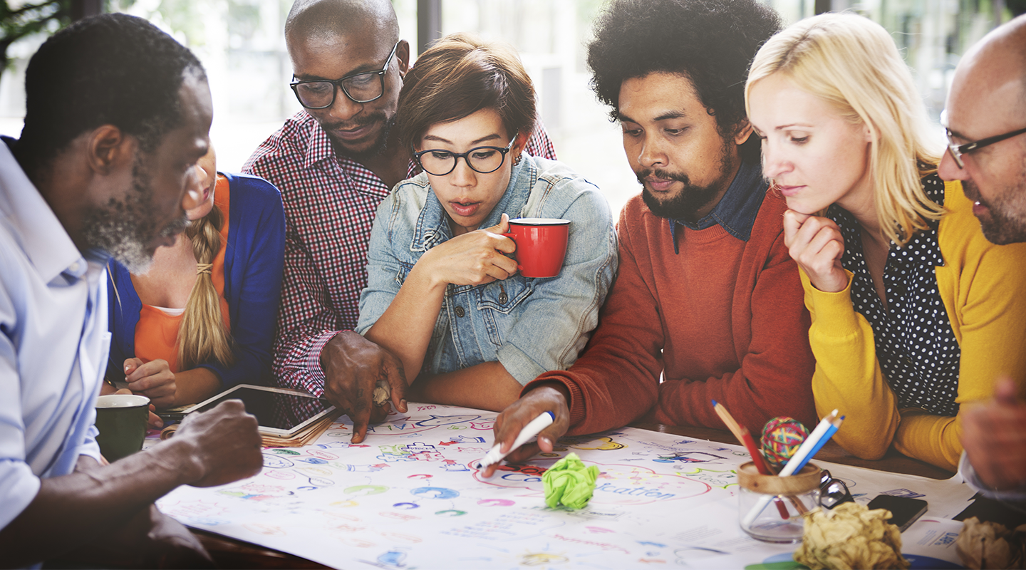 Public Relations professionals gathered around a table discussing a plan in real-time.